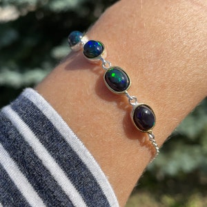 Può includere: Un braccialetto a catena d'argento con quattro pietre preziose di opale nero di forma ovale. Gli opali presentano un'iridescenza verde e blu.
