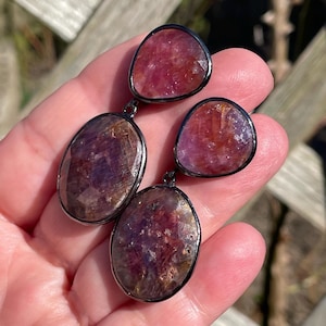 May include: A pair of dangle earrings with three faceted, oval-shaped, pink and purple gemstones set in silver.