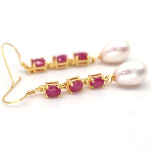 May include: Gold earrings with a row of pink oval gemstones and a dangling pearl drop.