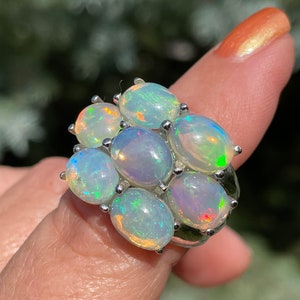 May include: A silver ring set with seven oval-shaped opals. The opals are iridescent and display a rainbow of colours.