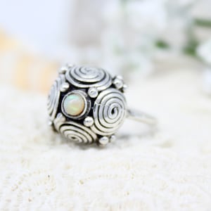 May include: A silver ring with a swirling design and a white opal gemstone in the center.
