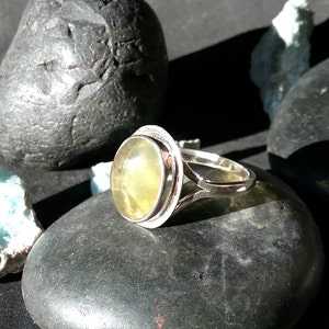 May include: A silver ring with a yellow oval gemstone set in a bezel setting. The ring has a delicate, openwork band.