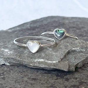 May include: Two silver rings with heart-shaped abalone shell inlays. One ring has a white abalone shell inlay, the other has a green and blue abalone shell inlay.