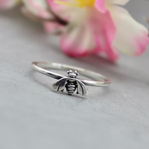 Può includere: Un anello d'argento con un designo a forma di ape. L'ape è dettagliata con ali, un corpo e gambe.