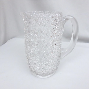 May include: Clear glass pitcher with a textured, starburst pattern. The pitcher has a curved handle and a spout for easy pouring. A classic piece for serving beverages.