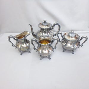 May include: A four-piece silver tea set consisting of a teapot with a lid, a lidded sugar bowl, a creamer, and a two-handled open sugar bowl. Each piece features a polished metallic finish, ornate curved handles, and decorative feet.