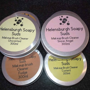 Può includere: Quattro barattoli rotondi in metallo di detergente per pennelli trucco Helensburgh Soapy Suds. Ogni barattolo ha un'etichetta di colore diverso: giallo, rosa, marrone e verde. Le etichette mostrano il nome del prodotto, la fragranza e il volume di 300 ml.