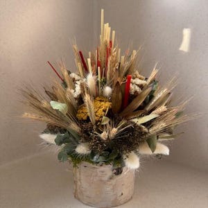 Könnte beinhalten: Ein dekoratives Arrangement aus getrockneten Blumen und Gräsern in einem Behälter aus Birkenrinde. Der Strauß zeigt Weizenähren, rote Akzente und verschiedene Texturen. Ein natürliches, rustikales Wohnaccessoire.