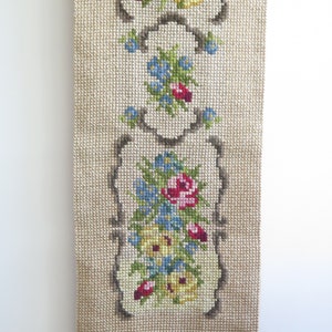 May include: A beige tapestry with a floral design featuring pink, red, yellow, and blue flowers. The tapestry has a fringe border.