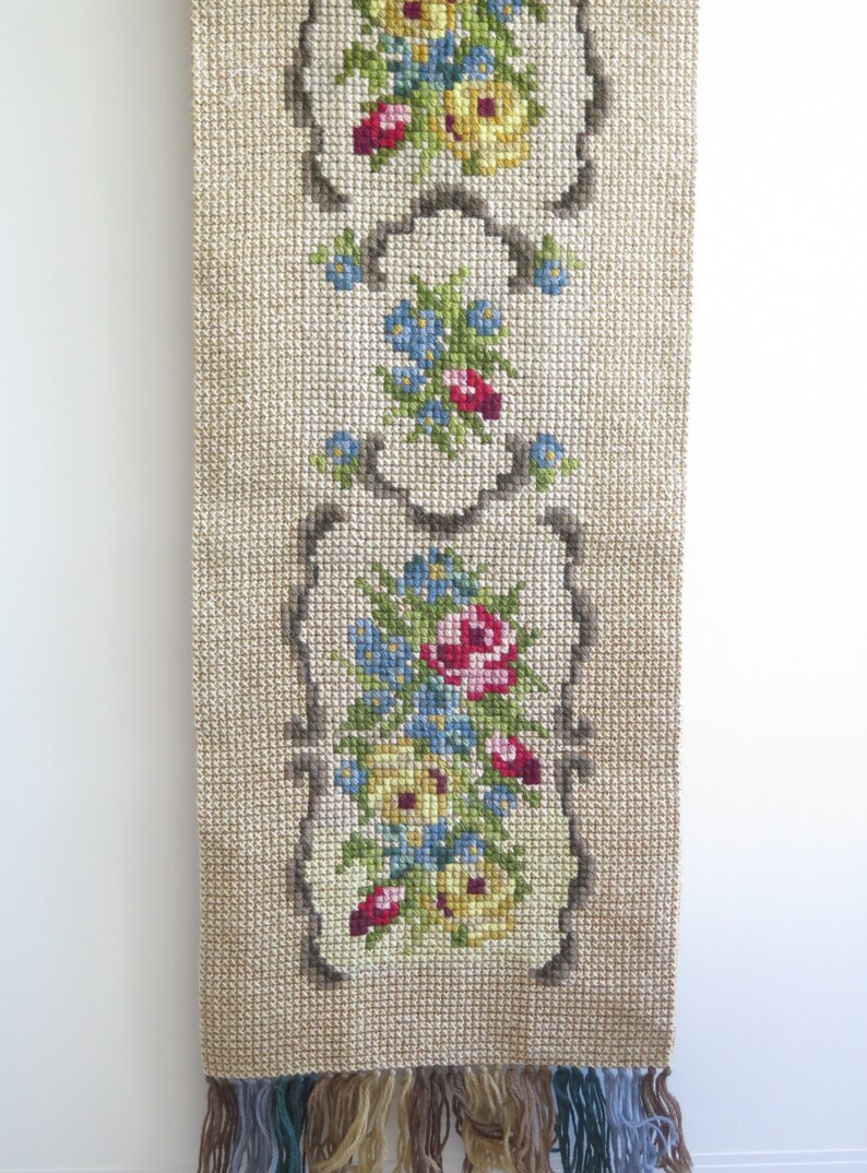 May include: A beige tapestry with a floral design featuring pink, red, yellow, and blue flowers. The tapestry has a fringe border.