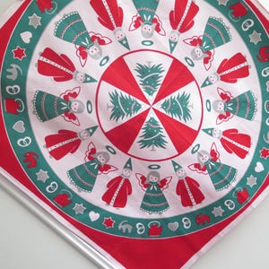 Könnte beinhalten: Ein runder, rot-weißer Weihnachtstischläufer mit einem sich wiederholenden Muster aus Engeln, Weihnachtsbäumen und festlichen Formen. Die Engel sind in Rot und Grün gekleidet, mit silbernen Heiligenscheinen und Hüten. Der Tischläufer hat einen roten Rand.