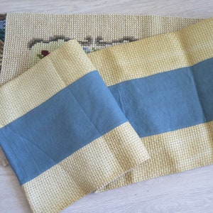 May include: A beige and blue striped runner with fringe on the ends. The runner is made of a woven fabric and has a subtle texture.