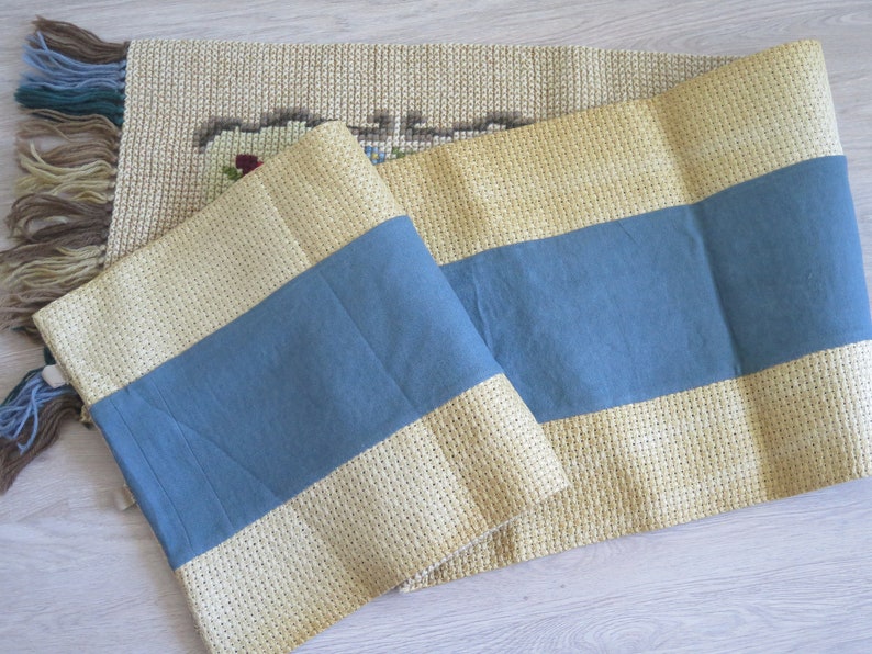 May include: A beige and blue striped runner with fringe on the ends. The runner is made of a woven fabric and has a subtle texture.