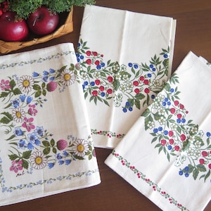 Può includere: Tre strofinacci di cotone bianco con un motivo floreale di bacche e foglie blu, rosse e verdi. Gli strofinacci hanno uno sfondo bianco e un bordo di piccoli fiori blu.