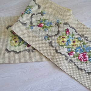 May include: Two beige embroidered table runners with floral designs. The runners have a fringe border and feature yellow, blue, red, and green flowers.