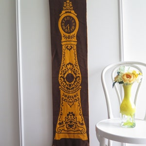 May include: A brown and gold fabric wall hanging with a clock face and intricate floral designs. The clock face has Roman numerals and black hands.