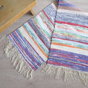 May include: A colorful woven rug with a fringe border. The rug has stripes of blue, red, green, orange, and white.