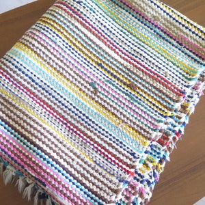 May include: A colorful striped woven rug with a fringe border. The rug is made of various colors including brown, blue, yellow, pink, and white.