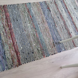 May include: A multi-colored woven rug with a striped pattern in shades of blue, red, green, and white. The rug is made of a thick, textured material and has a fringed edge.