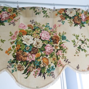 以下が含まれることがあります： クリーム色の花のバランスカーテン、スカラップエッジ付き。 バランスカーテンは、ピンク、白、オレンジ、茶色のバラの大きな中央の花束と、両側に小さな花の配置が特徴です。 生地はフリンジトリムで飾られています。
