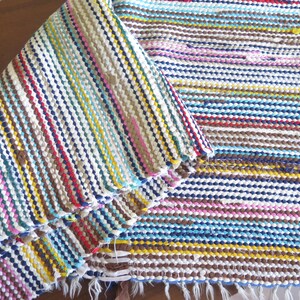 May include: A colorful woven rug with stripes of blue, yellow, pink, brown, and white. The rug is folded in half, showing the pattern on both sides.