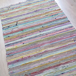 May include: Multicolored woven rug with horizontal stripes in shades of pink, blue, yellow, green, and brown. The rug has a frayed edge.