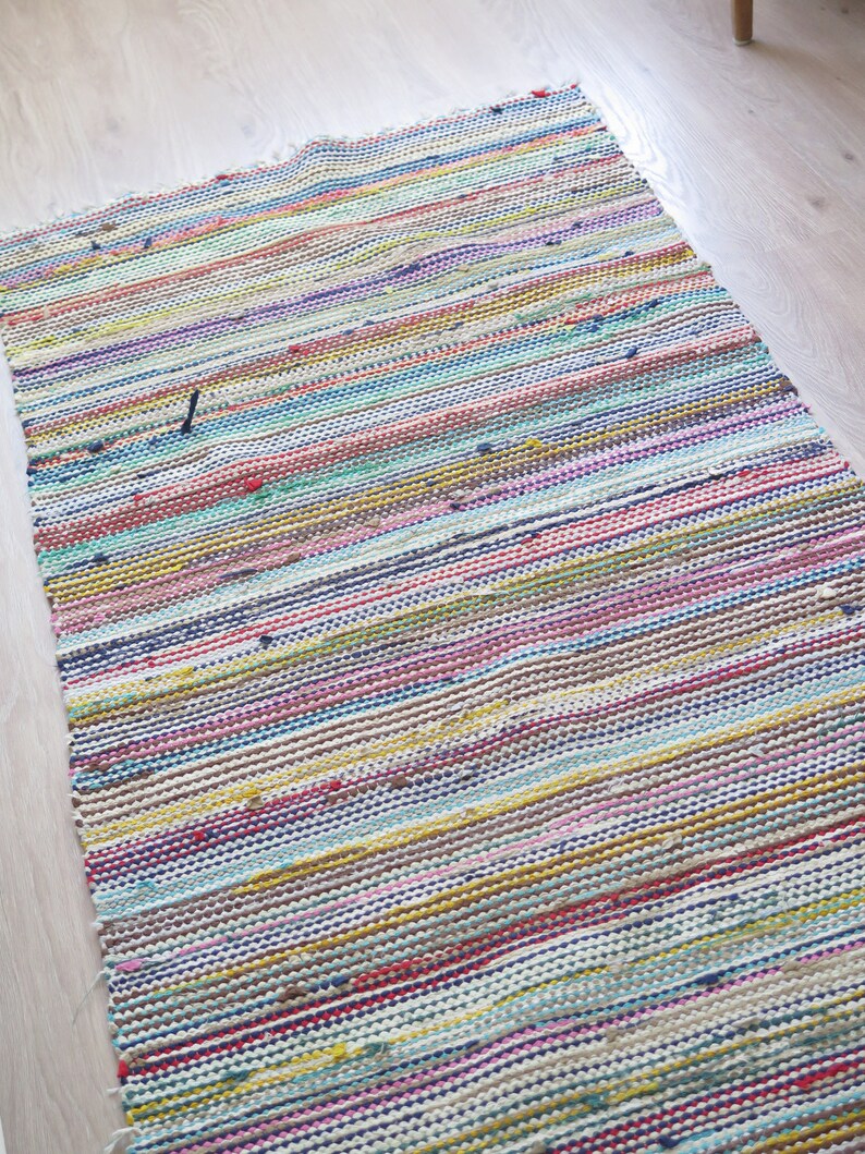 May include: Multicolored woven rug with horizontal stripes in shades of pink, blue, yellow, green, and brown. The rug has a frayed edge.