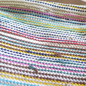 May include: A colorful striped woven rug with a variety of colors including brown, blue, yellow, pink, and white.