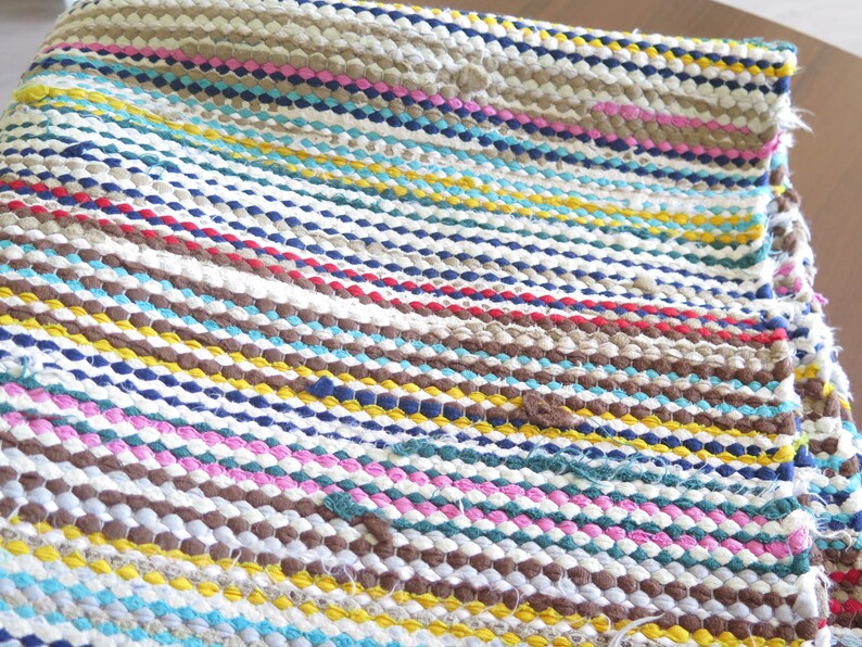May include: A colorful striped woven rug with a variety of colors including brown, blue, yellow, pink, and white.