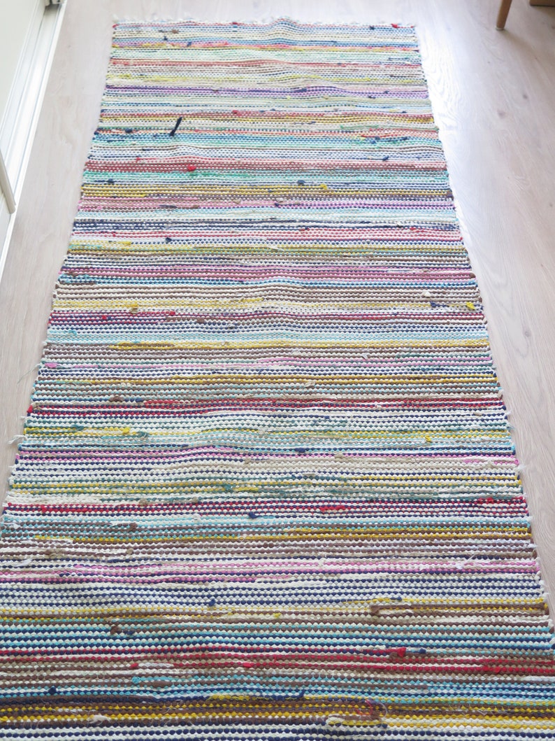 May include: A colorful striped rug with a woven texture. The rug is made of various colors, including blue, green, yellow, pink, and red.