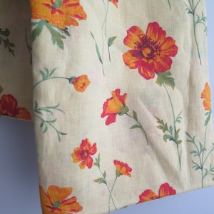 Può includere: Un tessuto color crema con un motivo floreale. I fiori sono arancioni e rossi con steli e foglie verdi.