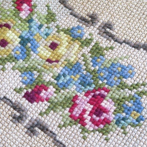 May include: Close-up of a beige fabric with embroidered flowers in shades of pink, red, yellow, blue, and green. The flowers are arranged in a symmetrical pattern.
