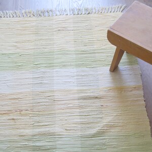 May include: A woven rug with a light green, white, and cream striped pattern. A wooden stool is partially visible in the upper right corner of the image.