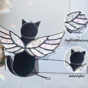 May include: Black cat with iridescent rainbow wings made of stained glass. The cat is sitting with its wings spread out behind it. The wings are made of stained glass and have a rainbow effect. The cat is hanging from a chain.