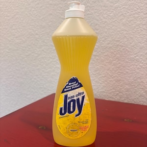 May include: A yellow translucent plastic bottle of non-ultra Joy dishwashing liquid with a white flip-top cap. The label features the text Great Cleaning! Great Price! and Joy in large blue letters, with lemon scent indicated in a volume of 12.6 fl oz.