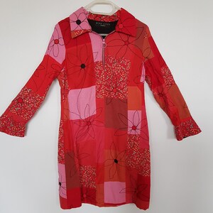 May include: A red and pink patterned dress with a zip fastening and a collar. The dress features a floral design with black outlines and red centres. The label on the dress reads "Miss Sixty" in black text.
