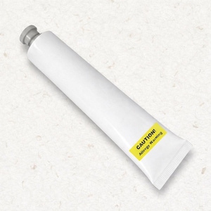 Peut inclure: Un tube souple blanc avec un bouchon gris, doté d'une étiquette rectangulaire jaune près de la base. L'étiquette porte le texte noir CAUTION! Allergy Warning. Le tube est placé en diagonale sur un fond blanc cassé légèrement texturé.