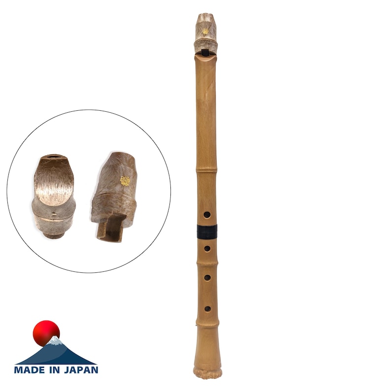 May include: A light brown bamboo flute with four finger holes, a black band, and a textured mouthpiece. A circular inset shows two views of the mouthpiece, which features a small gold-coloured emblem. The text "MADE IN JAPAN" is visible below.