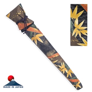 May include: A long, tapered fabric case for a sword or flute, featuring a dark charcoal background with a pattern of golden bamboo leaves, orange ribbons, and gold leaf accents. The top is secured with a dark purple braided cord tie.