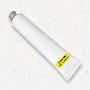 Può includere: Un tubetto bianco con tappo grigio dotato di un'etichetta rettangolare gialla con il testo nero CAUTION! Allergy Warning. Il tubetto è posizionato in diagonale e presenta una base sigillata a pressione, offrendo un design essenziale.