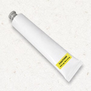 Peut inclure: Un tube souple blanc avec un bouchon gris, doté d'une étiquette rectangulaire jaune portant le texte noir CAUTION! Allergy Warning. Le tube est placé en diagonale et présente une base scellée par sertissage, offrant un design épuré.