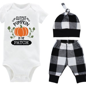 Puede incluir: Un conjunto de tres piezas para bebé con un body blanco, pantalones a cuadros blanco y negro y un gorro a cuadros blanco y negro. El body tiene un gráfico de calabaza y el texto "Cutest Pumpkin in the Patch".