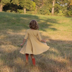 May include: A young person wearing a yellow dress with white polka dots and red tights spins in a grassy field.