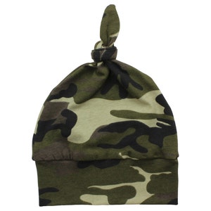 Puede incluir: Un gorro de beb&eacute; de camuflaje verde, marr&oacute;n y negro con un nudo en la parte superior.