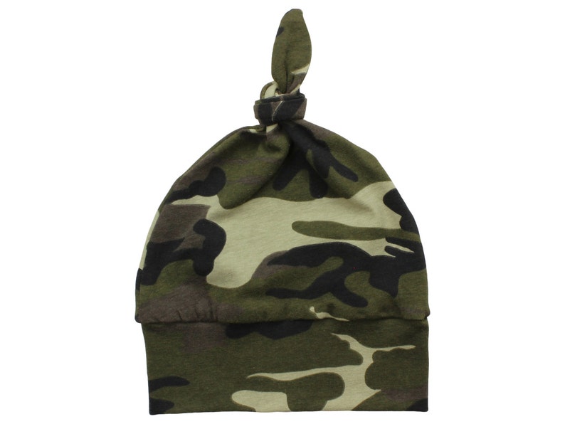 Puede incluir: Un gorro de beb&eacute; de camuflaje verde, marr&oacute;n y negro con un nudo en la parte superior.