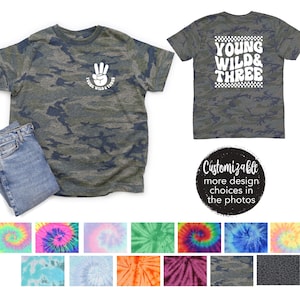 May include: A camouflage t-shirt with a white peace sign and the text "Young Wild & Three" on the front. The back of the shirt has the text "Young Wild & Three" in a checkered pattern. The shirt is customizable with different colors and patterns.