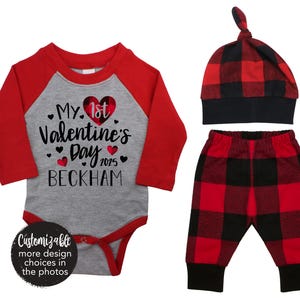 May include: Red and grey baby onesie with the text "My 1st Valentine's Day 2025 Beckham". A red and black checked hat and trousers complete the outfit.