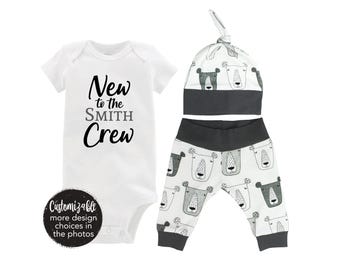 Könnte beinhalten: Ein weißer Baby-Strampler mit dem Text "New to the SMITH Crew". Eine weiße und graue Baby-Mütze mit einem Bärenkopf-Design. Weiße und graue Baby-Hosen mit einem Bärenkopf-Design.