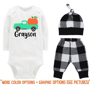 May include: A white long-sleeve bodysuit with a green truck carrying a pumpkin and the name "Grayson" printed on the front. The outfit also includes black and white checkered pants and a black and white checkered hat.