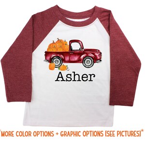 May include: A white and maroon long-sleeved baseball tee shirt with a red truck carrying pumpkins and the name "Asher" printed on the front.
